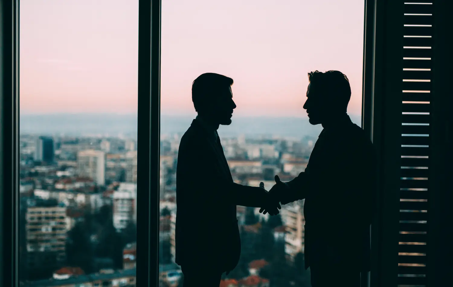 Two men shaking hands next to a floor to ceiling windows city