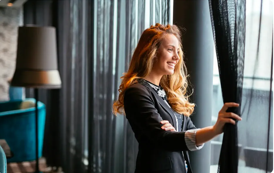 Professional woman standing by a window in a modern office, representing executive confidence, privacy and corporate security.