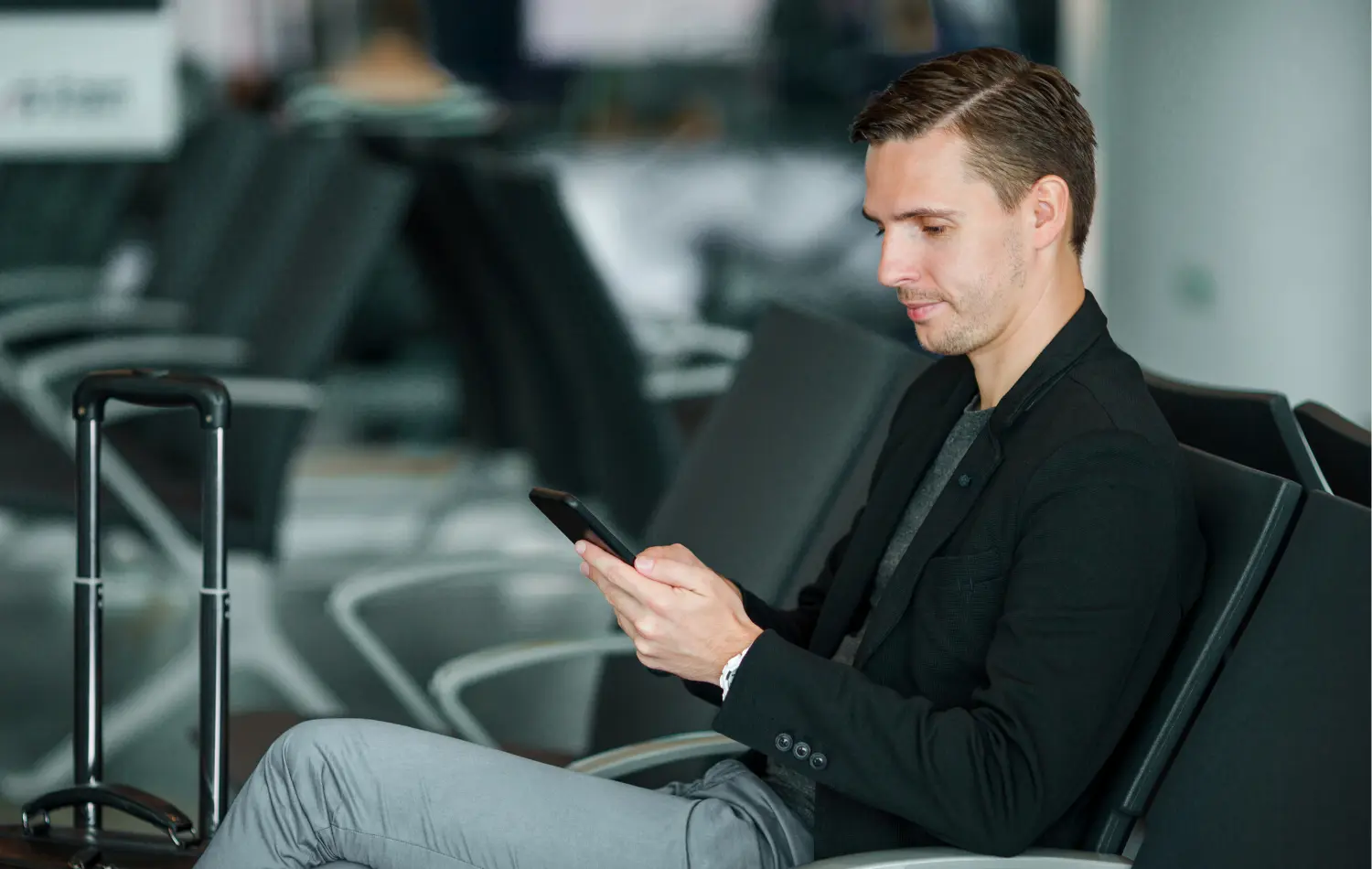 An employee at their airport sitting in the waiting area for a business trip looking at their phone