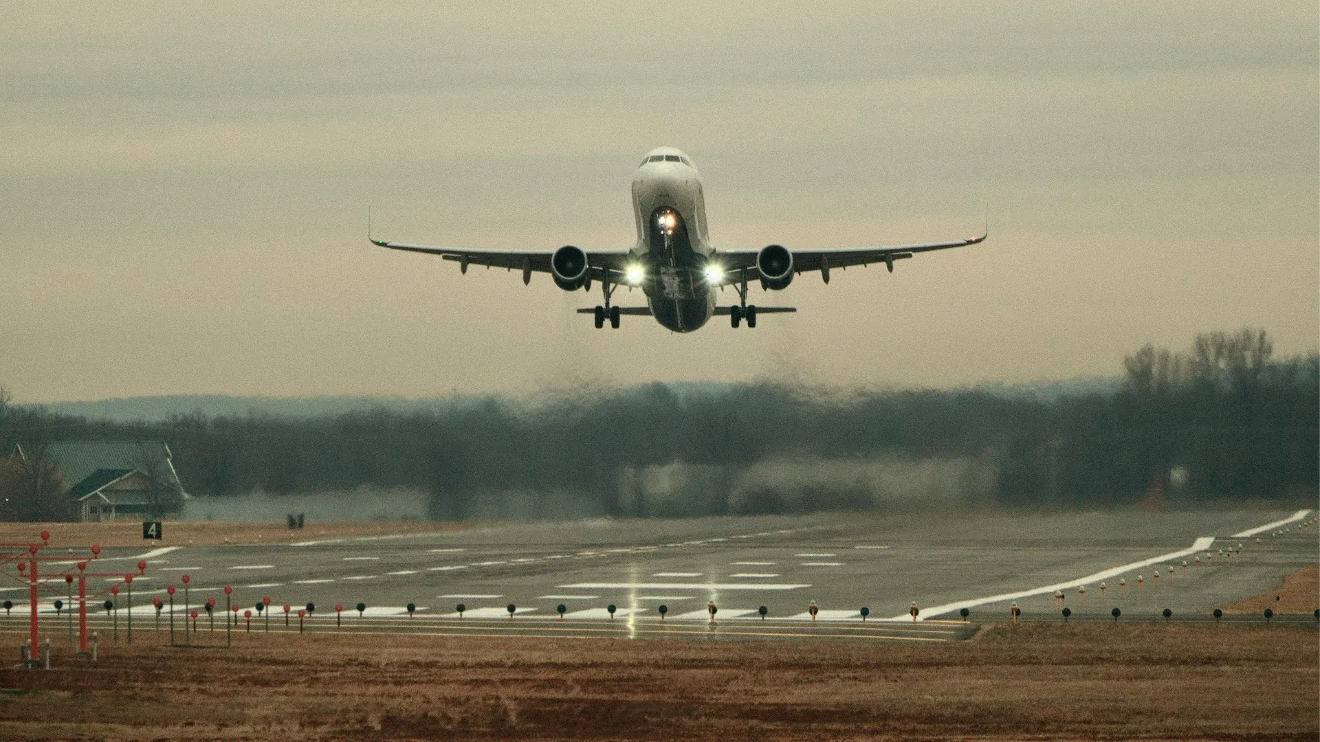 An airplane approaching the runway for landing at an airport during hazy weather, with landing lights on and runway lights visible.