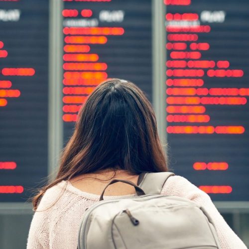 Rearview shot of an unrecognizable young woman looking at an arrivals and departures board while standing in an airport.